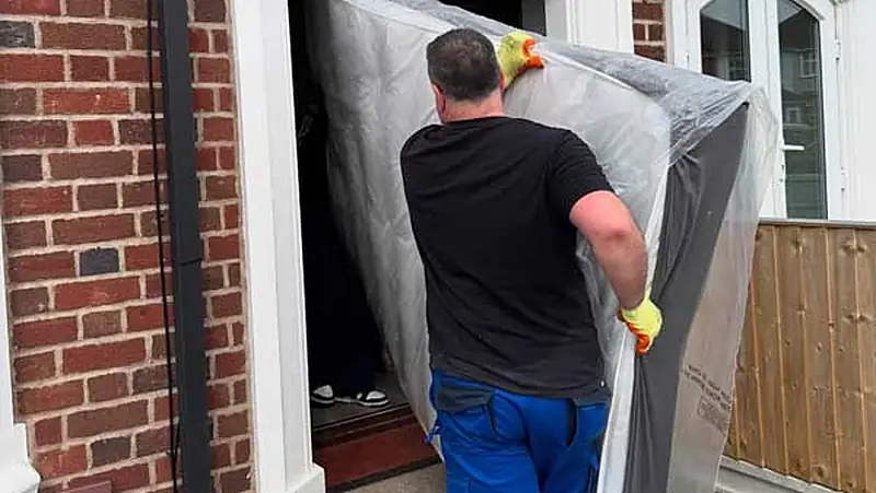 Military Movers UK crew carrying a protected mattress through a front door during a house removal