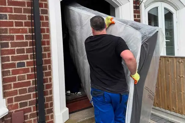 Military Movers UK crew carrying a protected mattress through a front door during a house removal