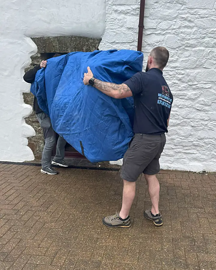 Military Movers UK removals crew carrying blanket-wrapped furniture during a house move