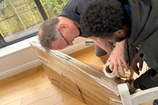 Two Military Movers UK packers wrapping a protected item in stretch film before a move